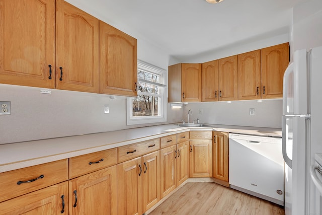 kitchen with a sink, white appliances, light wood-style flooring, and light countertops