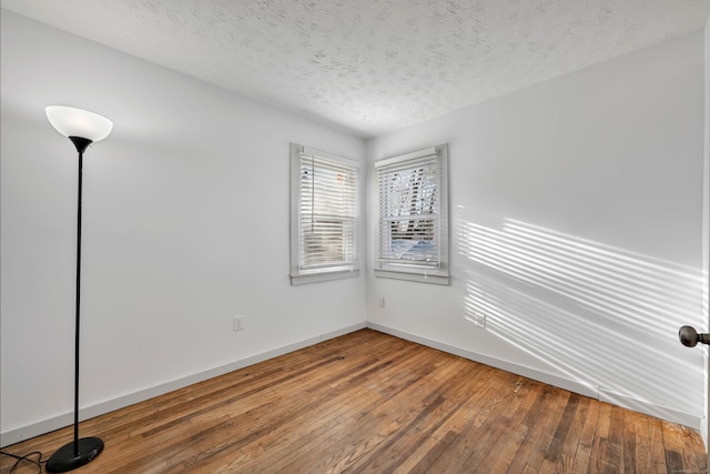 spare room with hardwood / wood-style floors, baseboards, and a textured ceiling