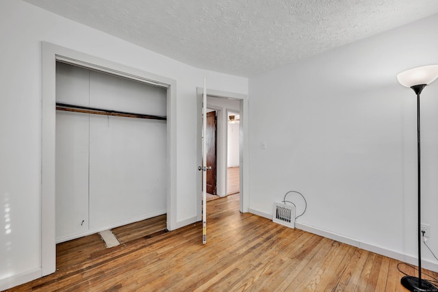 unfurnished bedroom featuring baseboards, visible vents, a closet, wood-type flooring, and a textured ceiling