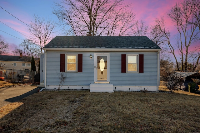 bungalow-style home featuring roof with shingles, a yard, and fence