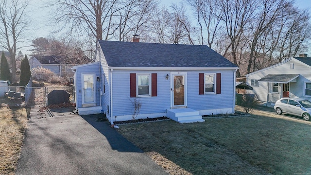 bungalow-style house featuring entry steps, fence, a front yard, a shingled roof, and a chimney