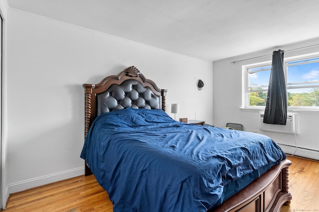 bedroom featuring cooling unit, a baseboard heating unit, baseboards, and wood finished floors