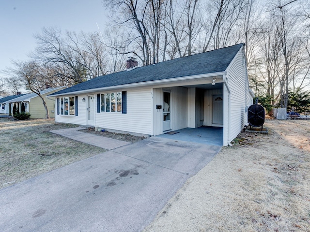 single story home featuring an attached carport, roof with shingles, driveway, and a chimney