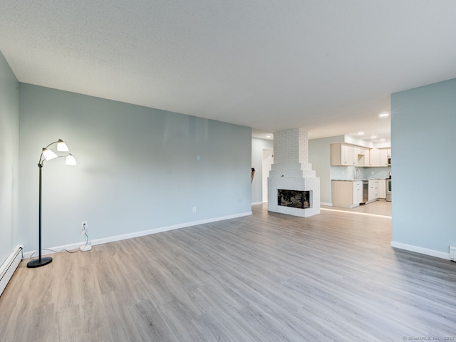 unfurnished living room featuring a baseboard heating unit, baseboards, light wood-style flooring, and a fireplace