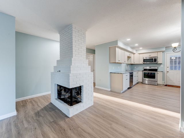 kitchen featuring light wood finished floors, baseboards, a fireplace, stainless steel appliances, and a sink