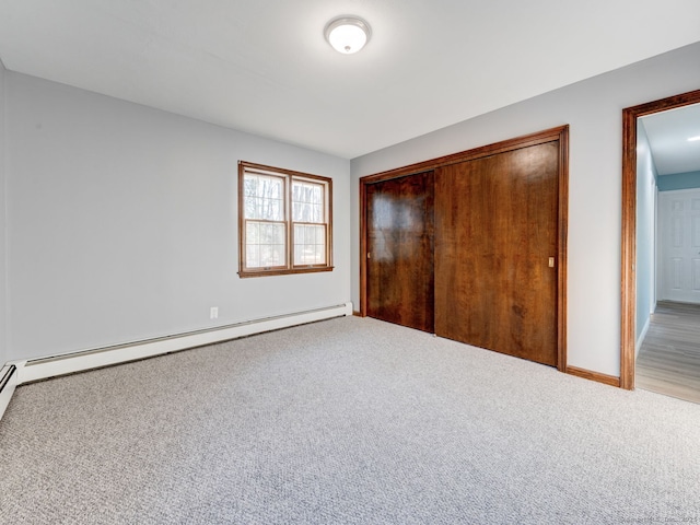 unfurnished bedroom with a baseboard heating unit, baseboards, carpet, and a closet