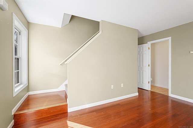 unfurnished living room featuring stairway, baseboards, a healthy amount of sunlight, and wood finished floors