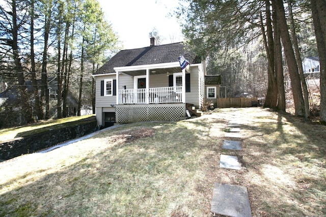 view of front of property featuring a chimney, a front lawn, a porch, and roof with shingles