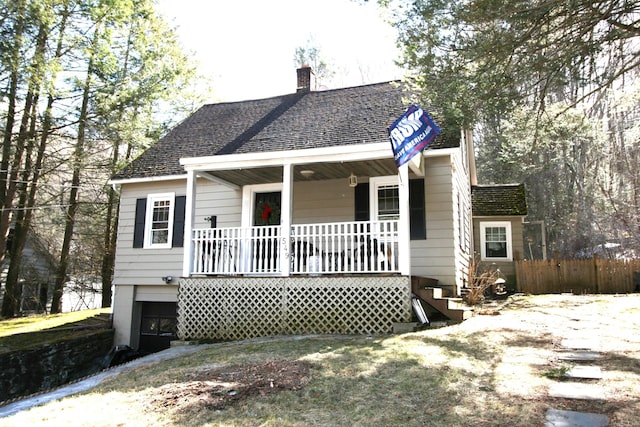 view of front of house with covered porch, a chimney, fence, and roof with shingles