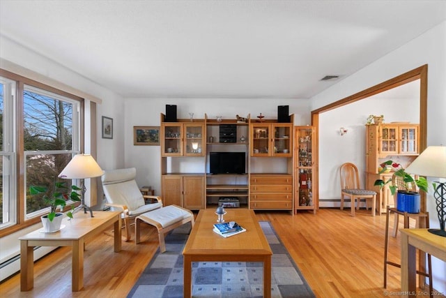 living room featuring light wood-style floors, a baseboard radiator, and visible vents