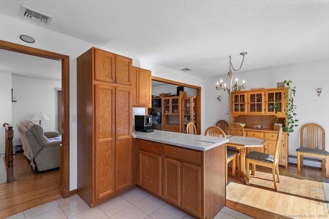 kitchen featuring a baseboard heating unit, a peninsula, visible vents, light countertops, and brown cabinetry