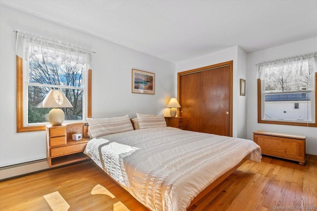 bedroom featuring a closet, baseboard heating, and wood finished floors