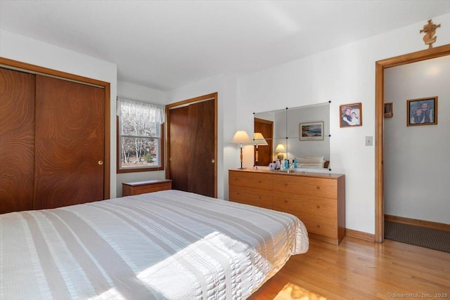 bedroom featuring two closets, light wood-style flooring, and baseboards