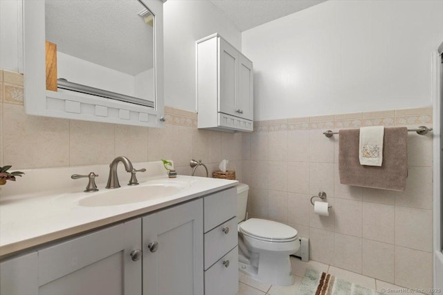 bathroom featuring a textured ceiling, tile patterned flooring, toilet, vanity, and tile walls