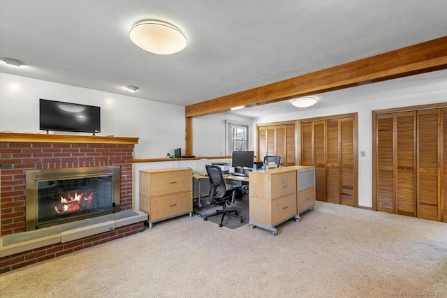 office area with a brick fireplace, beam ceiling, and light colored carpet