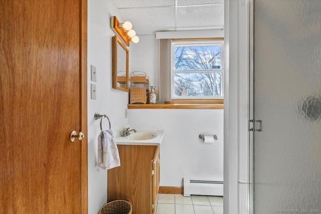 bathroom with a paneled ceiling, a baseboard heating unit, a shower with shower door, vanity, and tile patterned floors