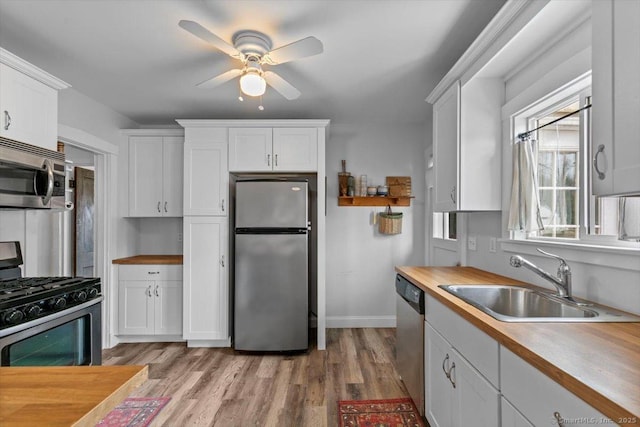 kitchen featuring wooden counters, light wood-style flooring, appliances with stainless steel finishes, white cabinets, and a sink