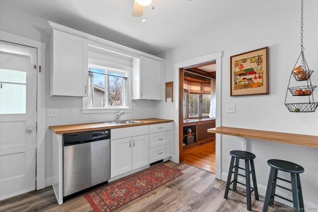 kitchen featuring light wood-type flooring, stainless steel dishwasher, white cabinetry, wooden counters, and a sink