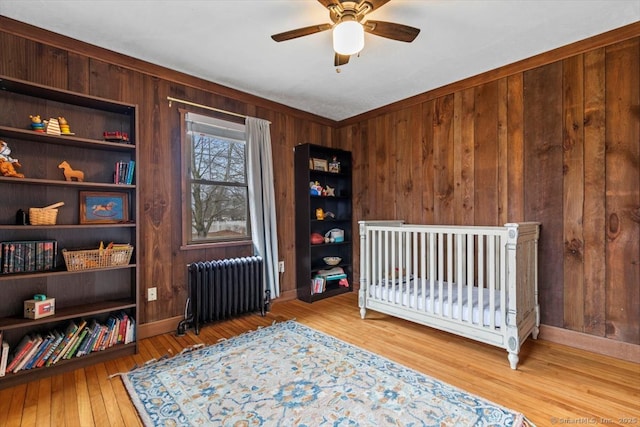 bedroom with baseboards, hardwood / wood-style floors, radiator heating unit, and wooden walls