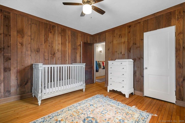 bedroom with hardwood / wood-style flooring, ceiling fan, wooden walls, and baseboards