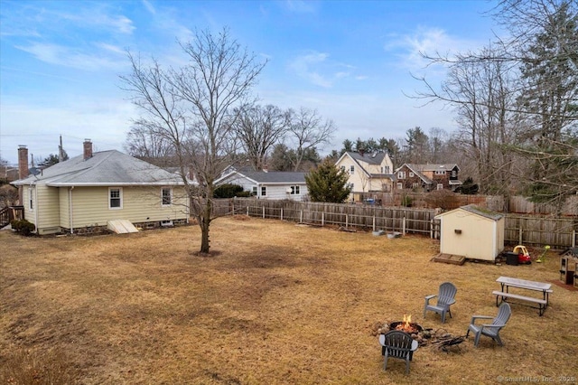 view of yard with a storage shed, a fenced backyard, a fire pit, and an outdoor structure