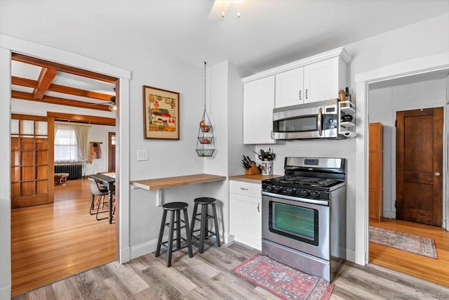 kitchen with baseboards, white cabinets, radiator, stainless steel appliances, and light wood-style floors