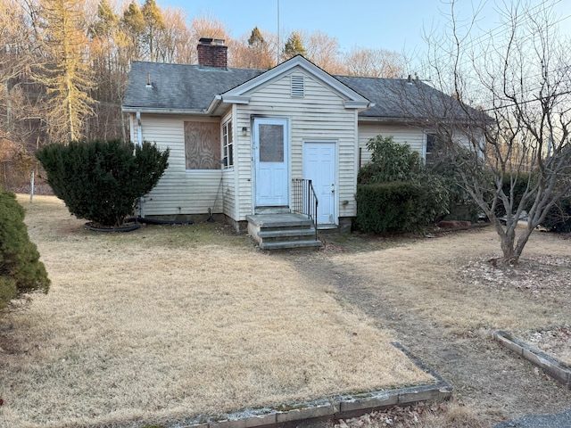 view of front of house featuring a front yard, roof with shingles, and a chimney