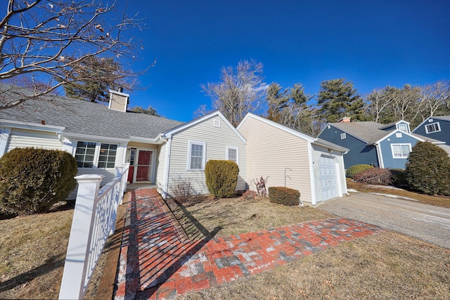 view of front of property with driveway, a chimney, an attached garage, and roof with shingles