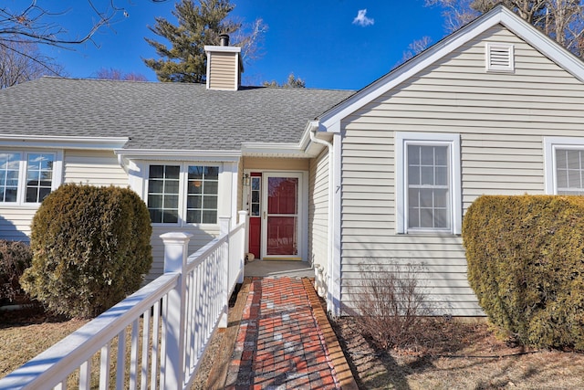 entrance to property featuring a shingled roof and a chimney