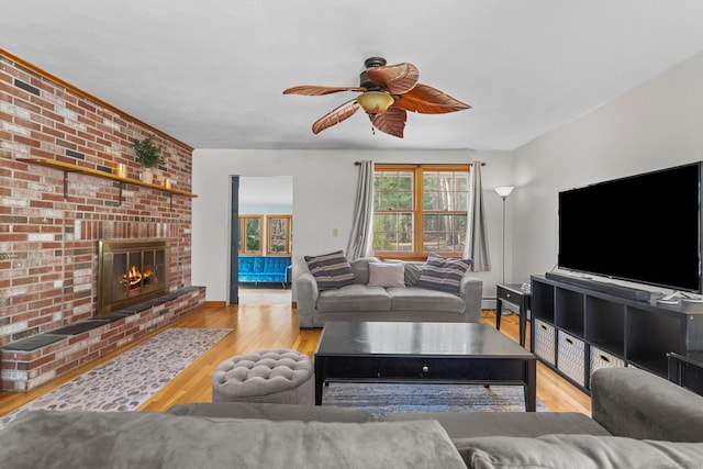 living area with a brick fireplace, wood finished floors, baseboards, and ceiling fan