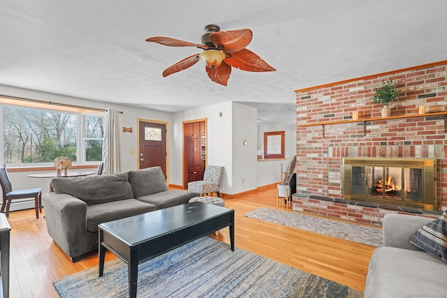 living room featuring ceiling fan, baseboards, light wood-style flooring, and a fireplace