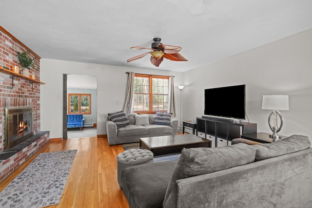 living area featuring a ceiling fan, baseboards, a fireplace, light wood-type flooring, and baseboard heating