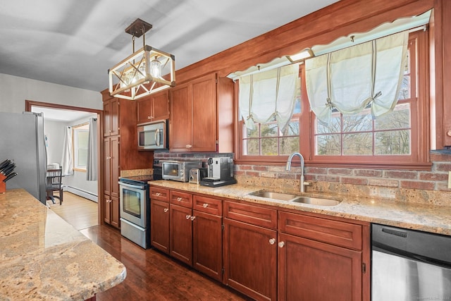 kitchen with dark wood-style floors, stainless steel appliances, a sink, a baseboard heating unit, and decorative light fixtures