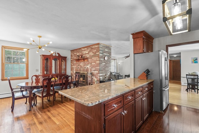 kitchen featuring a peninsula, light wood-style flooring, a fireplace, and freestanding refrigerator