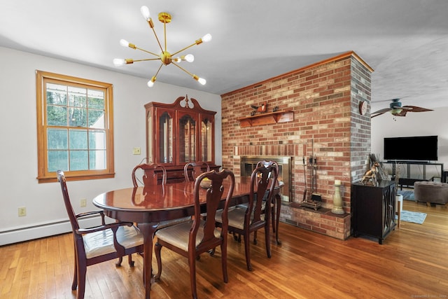 dining room featuring ceiling fan with notable chandelier, a brick fireplace, a baseboard heating unit, and hardwood / wood-style floors