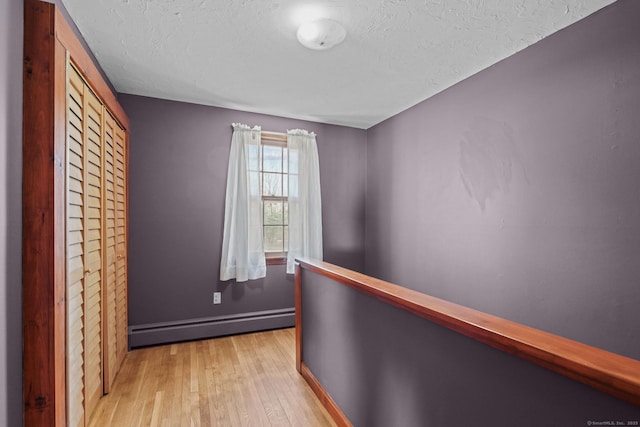 interior space featuring a textured ceiling, baseboards, light wood-type flooring, and a baseboard radiator