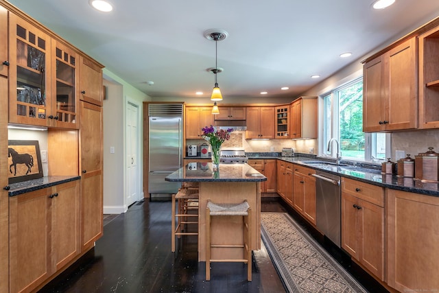 kitchen featuring a sink, a kitchen island, backsplash, appliances with stainless steel finishes, and dark wood-style flooring