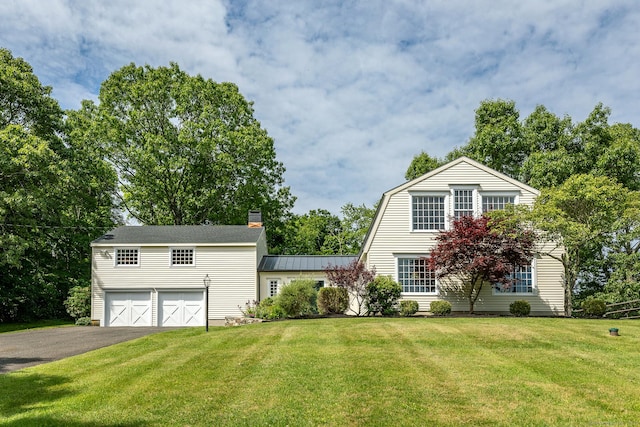 view of front of house with a front lawn, aphalt driveway, a gambrel roof, metal roof, and an attached garage