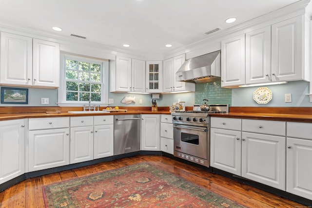 kitchen featuring visible vents, a sink, appliances with stainless steel finishes, white cabinets, and wall chimney range hood