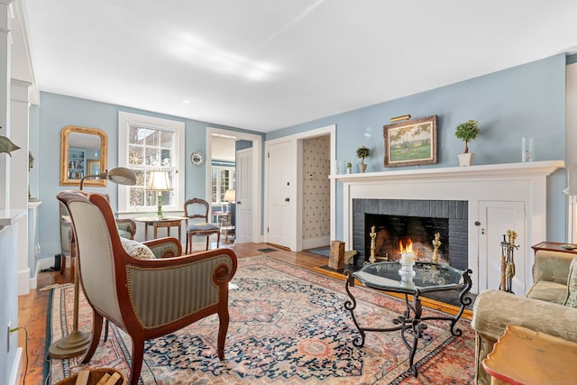 living room featuring baseboards, a brick fireplace, and wood finished floors