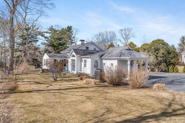 view of front of house with driveway, a chimney, a front yard, and a shingled roof