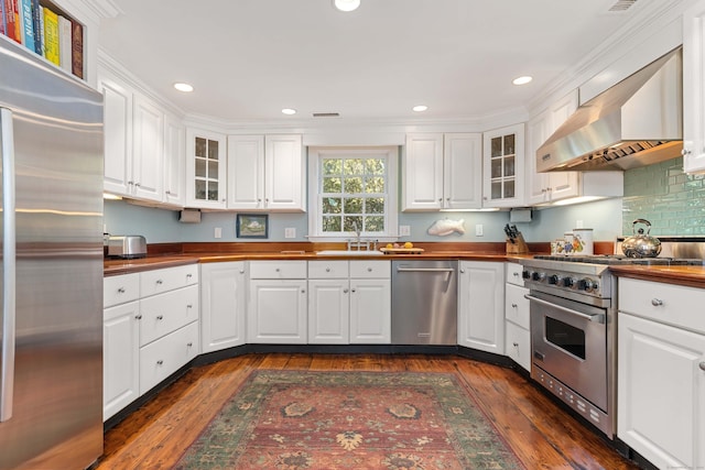 kitchen featuring wood counters, white cabinetry, high end appliances, and wall chimney range hood