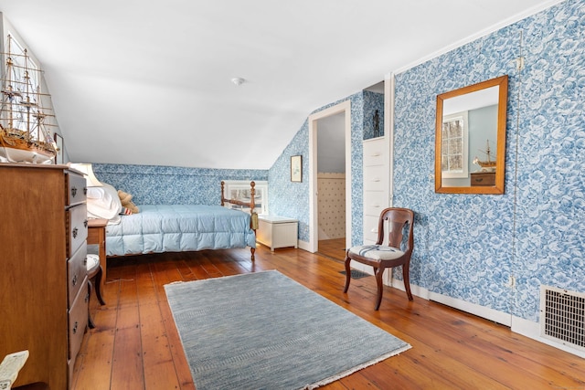 bedroom with baseboards, visible vents, wallpapered walls, hardwood / wood-style flooring, and vaulted ceiling