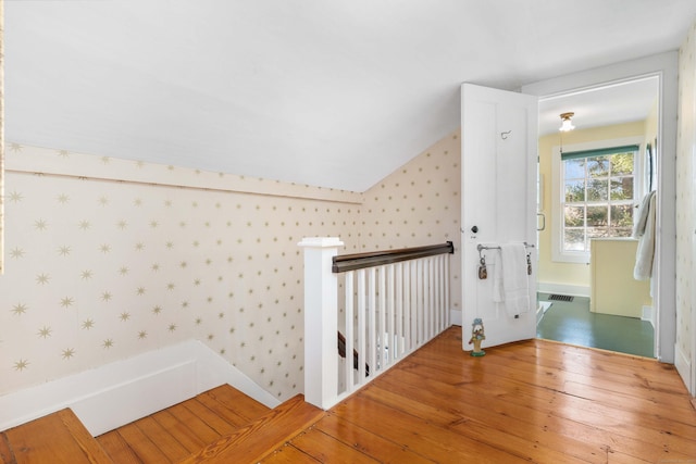 corridor featuring visible vents, wallpapered walls, lofted ceiling, an upstairs landing, and wood-type flooring