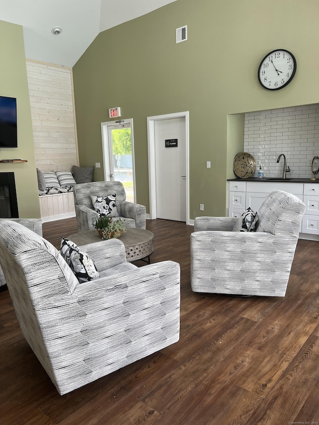 living area with visible vents, dark wood finished floors, baseboards, a glass covered fireplace, and high vaulted ceiling