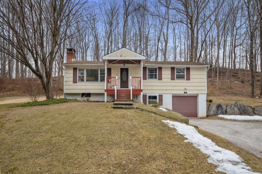 view of front of property featuring a front yard, driveway, a chimney, and an attached garage