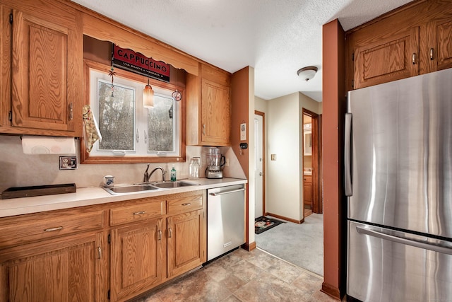 kitchen featuring a textured ceiling, a sink, light countertops, appliances with stainless steel finishes, and brown cabinets