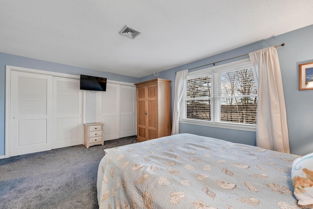 bedroom featuring carpet, visible vents, a textured ceiling, and two closets