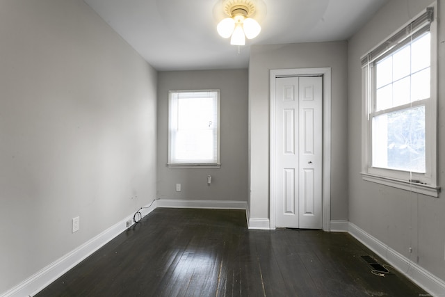 unfurnished bedroom with dark wood-type flooring, a closet, multiple windows, and baseboards