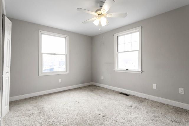 carpeted spare room with visible vents, baseboards, and ceiling fan